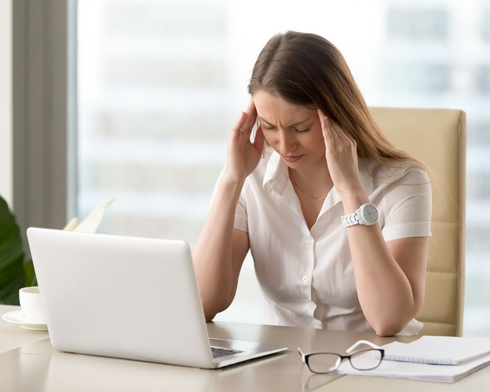 A woman holding her head with both hands, eyes closed, experiencing a tension headache